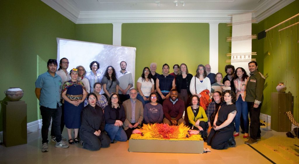 Group photo of approximately two dozen people posed in an art gallery with green walls.