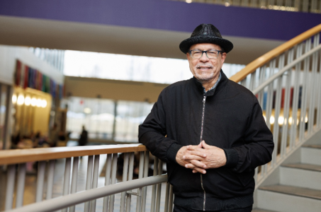 Professor Jose Cruz wearing a hat and jacket stands confidently on a stairway, looking straight with a slight smile. 
