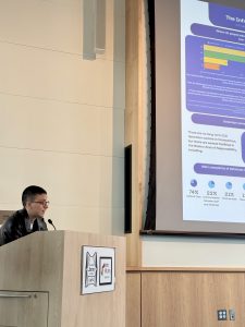 Graduate student presents at a podium, engaging with the audience during a formal event.