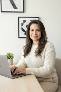 A woman seated at a desk, focused on her laptop, with a notepad and pen beside her.