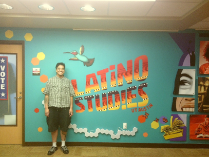 Graduate student, Julien, stands in front of a vibrant Latino studies mural from UT Austin, showcasing cultural themes and artistic expression.
